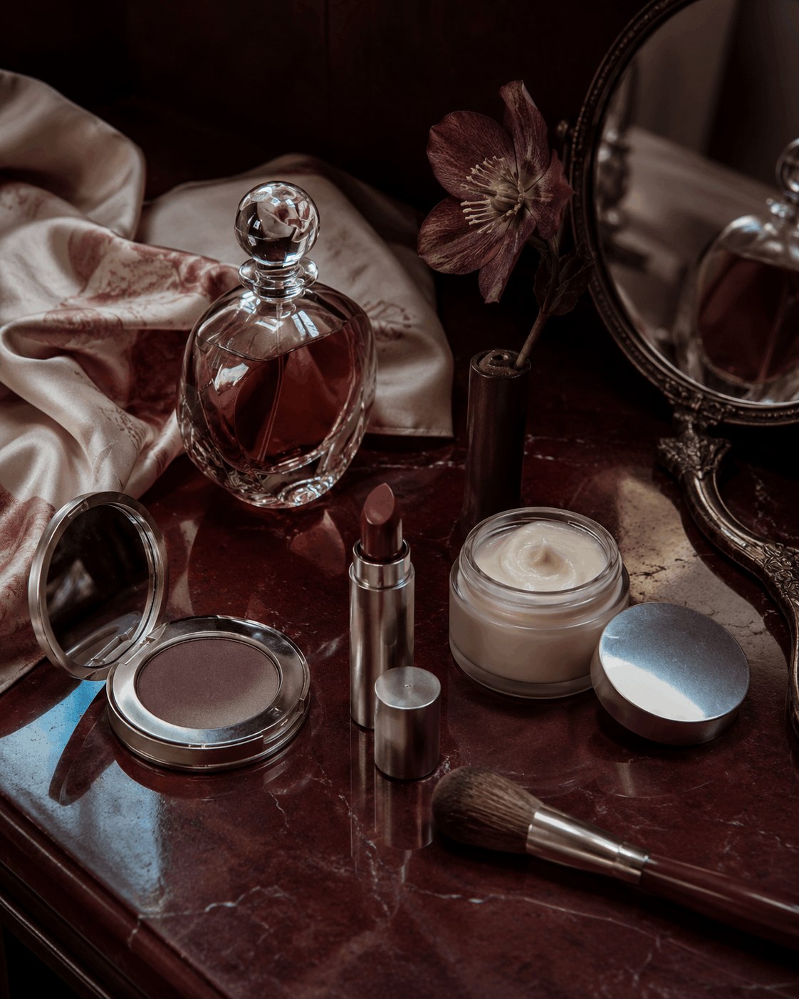 Perfume, makeup and powder arranged on dark red silk