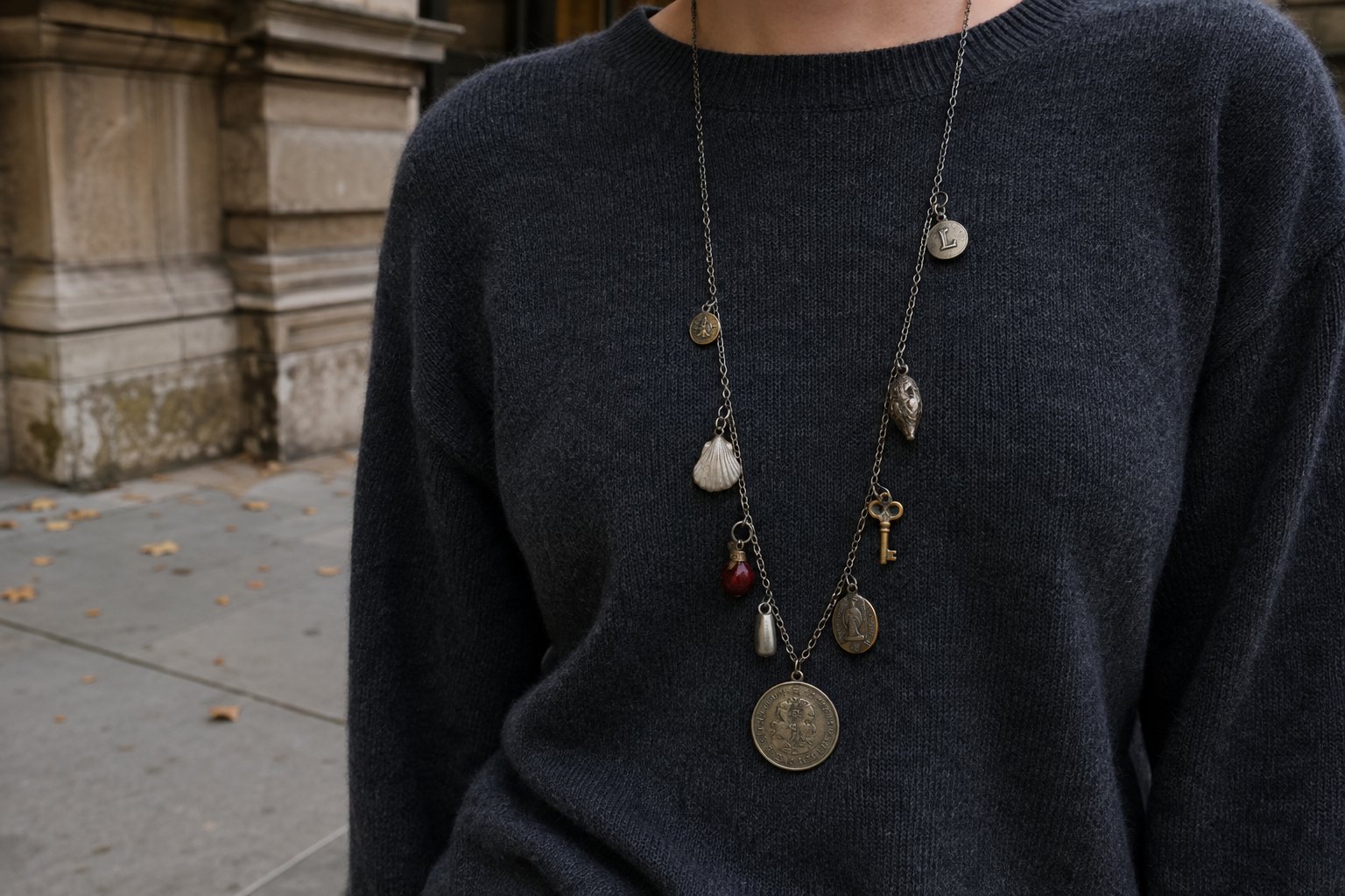 Long eclectic necklace with old medallions, small keys, shells and enamel charms worn over a plain charcoal knit, cropped from chin to waist